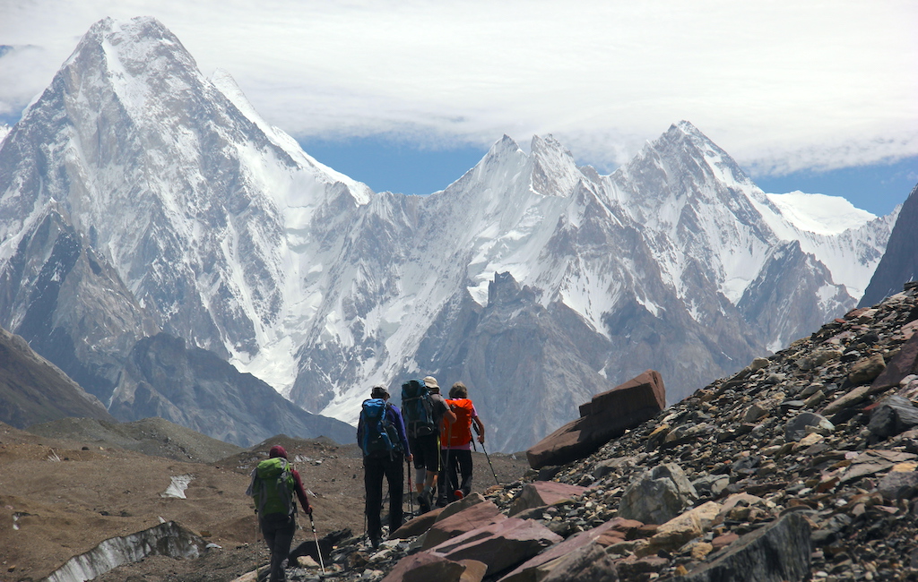 Eine Gruppe Wanderer beim Trekking auf dem Baltoro-Gletscher mit schneebedeckten Berggipfeln als imposanten Hintergrund.
